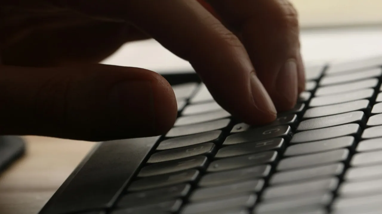 Hands typing on a compact keyboard in front of a softly blurred display