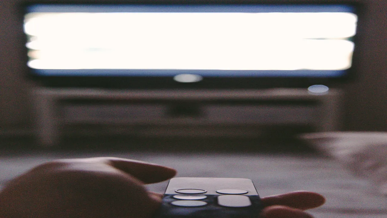 Close-up of a television remote control resting in front of an abstract guide screen