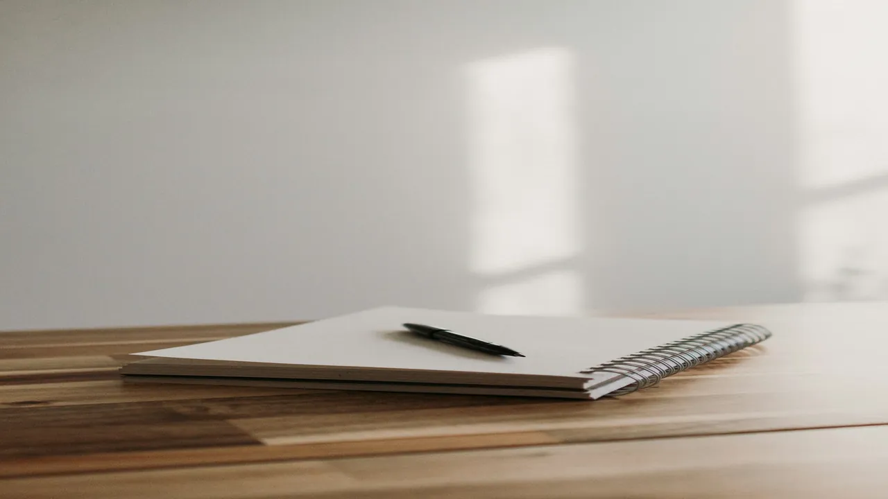 Notebook with a pen and remote control on a wooden table